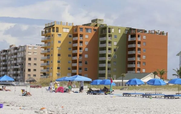 A beachfront hotel with multiple floors, balconies, and beach umbrellas.