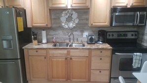 A kitchen with wooden cabinets, a stainless steel refrigerator, a microwave, a toaster, and a sink.
