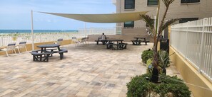 A patio area with picnic tables and chairs, a shaded area, and a view of the ocean.