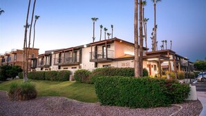 A multi-story hotel with balconies, palm trees, and a well-maintained lawn.