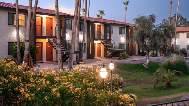 Ein mehrstöckiges Hotel mit rotem Ziegeldach, zahlreichen Balkonen und einem gepflegten Garten mit gelben Blumen.