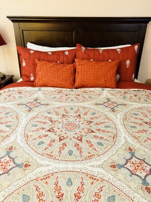 A bed with a patterned bedspread and two red pillows with white embroidery. - Upscale Fully Furnished Condo for Monthly Vacation Rentals (Palm Springs)