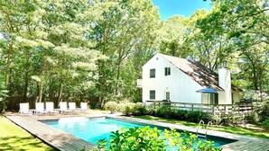 Una casa con piscina, rodeada de árboles y una terraza de madera.