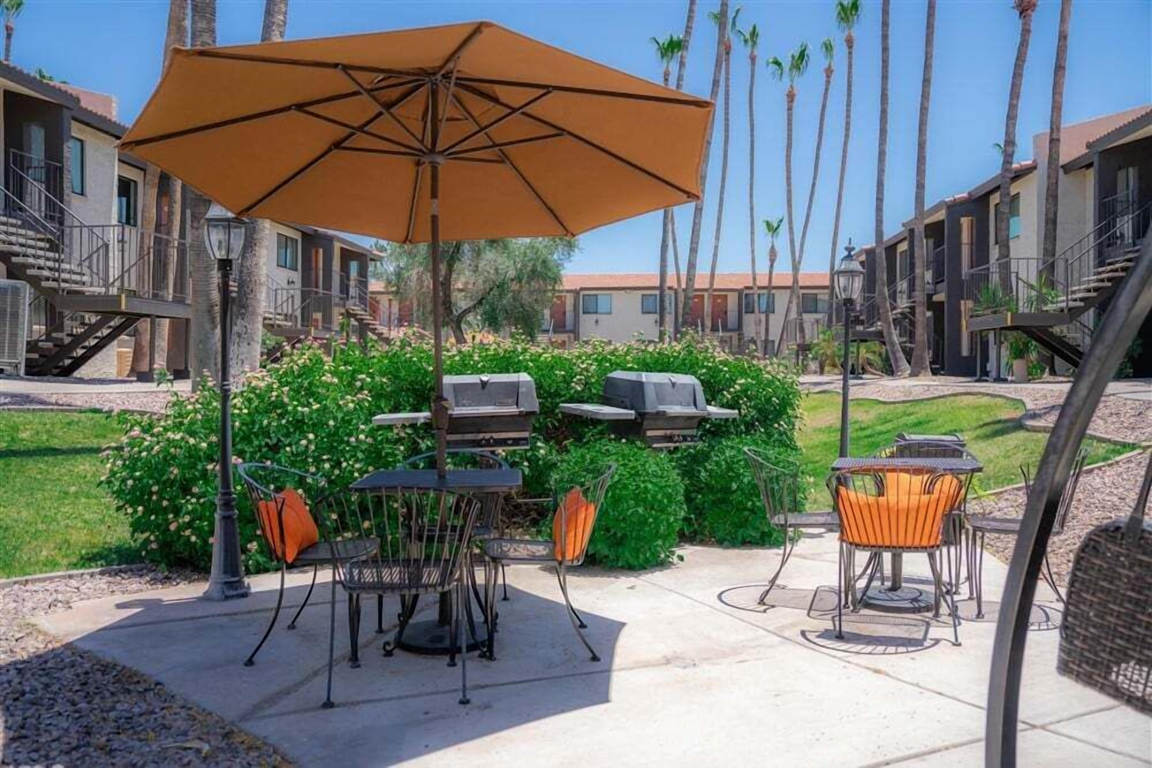 Un espace patio avec des sièges d’extérieur, un barbecue et un grand parasol.