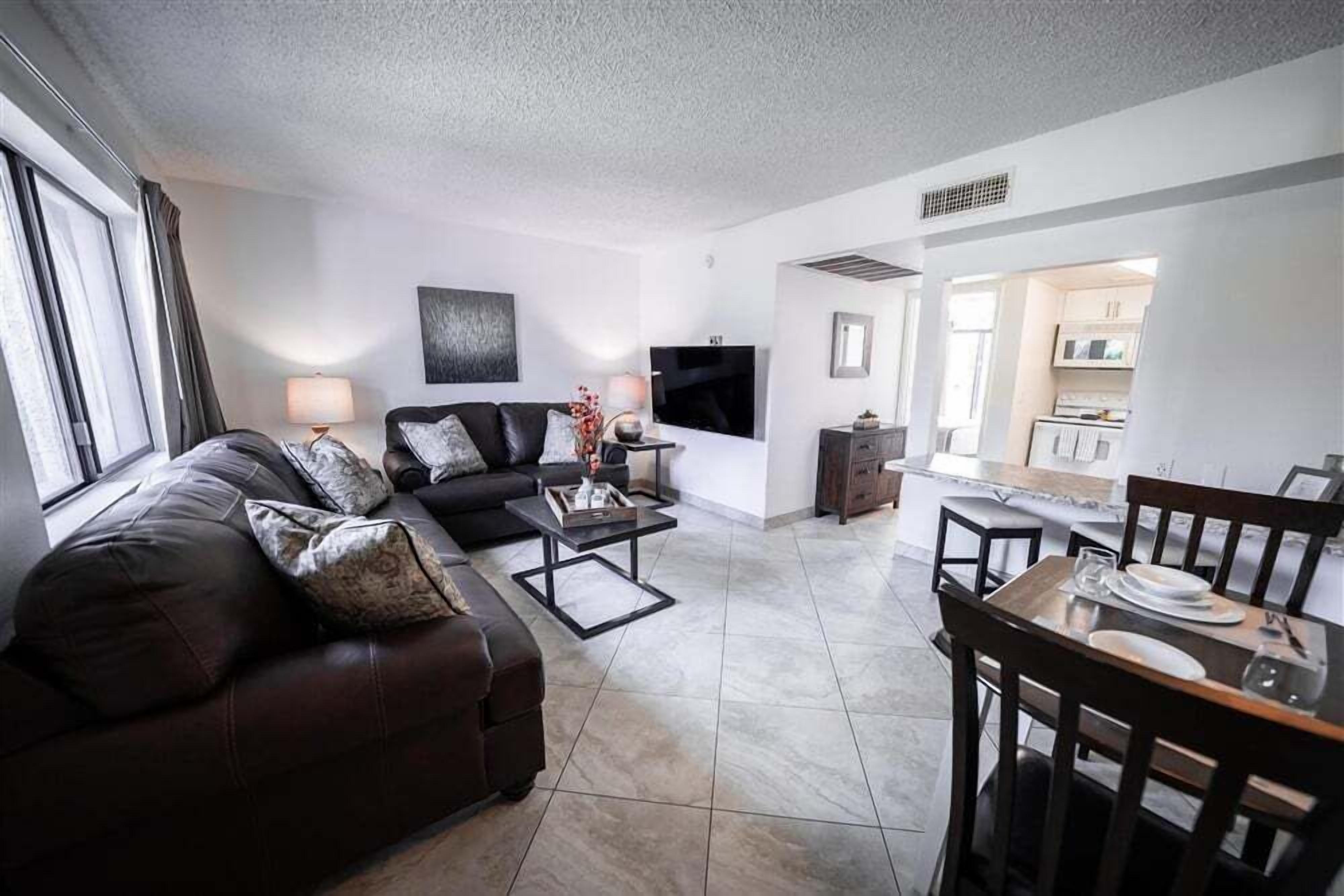 A modern living room with a sofa, coffee table, TV, and dining area.
