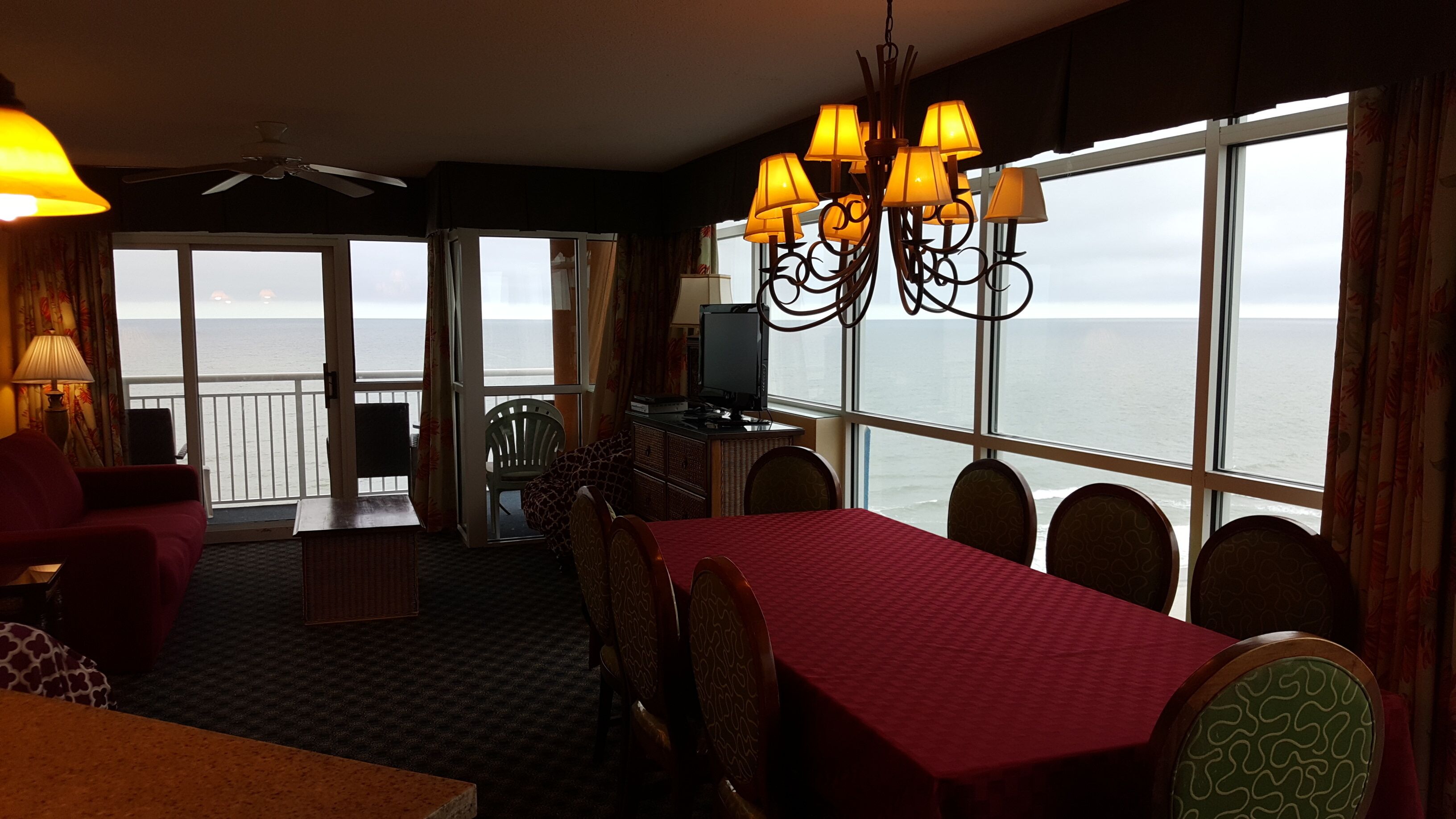 Une pièce comprenant une table à manger, des chaises, un téléviseur et donnant sur la mer.