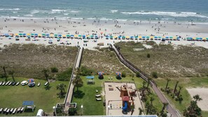 A beach with numerous umbrellas and sun loungers, a boardwalk, and a playground area.
