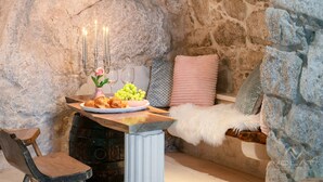 Une pièce aux murs de pierre, avec une table en bois dressée pour un repas, comprenant une assiette de nourriture, un vase avec des fleurs et un chandelier.