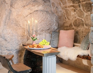 Une pièce aux murs de pierre, avec une table en bois dressée pour un repas, comprenant une assiette de nourriture, un vase avec des fleurs et un chandelier.