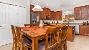A modern kitchen with wooden cabinets, stainless steel appliances, and a dining area with a wooden table and chairs. - Serene Pool Home Overlooking Conservation Area 🌳🏊‍♂️ (Davenport)