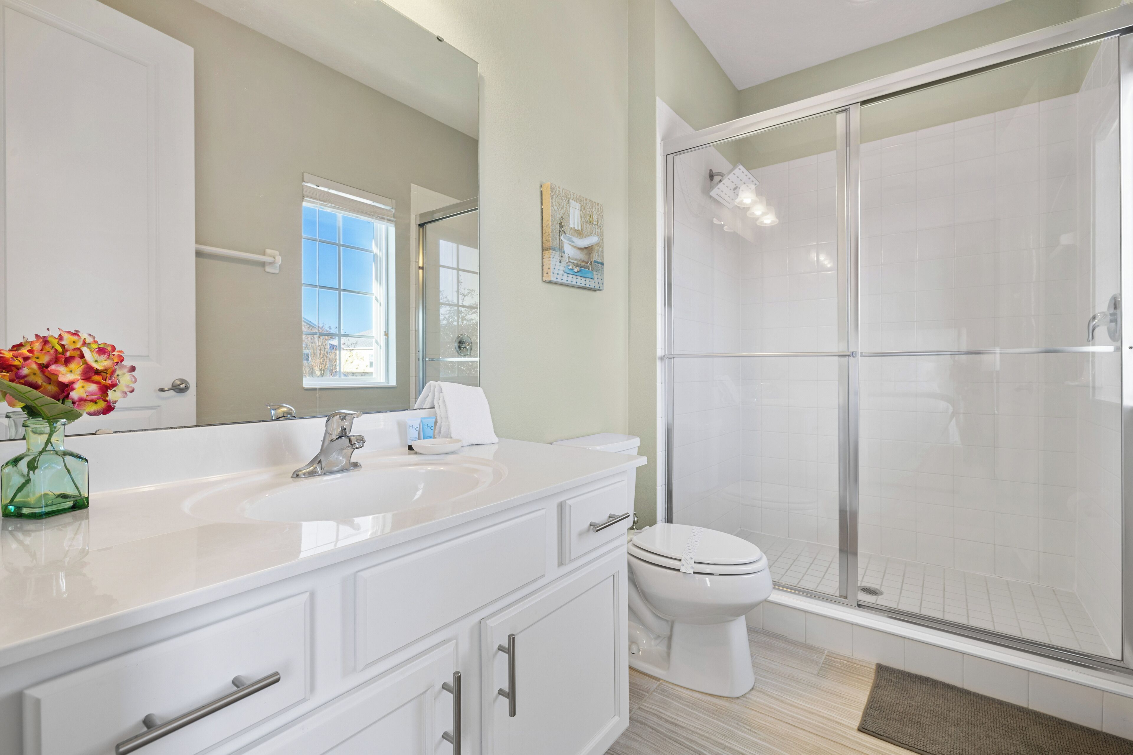Une salle de bain moderne avec un grand miroir, un meuble-lavabo blanc et une cabine de douche en verre.