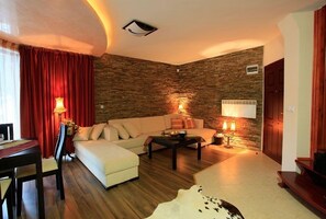 A cozy living room with a stone wall, a sofa, a coffee table, and a dining area with a table and chairs.