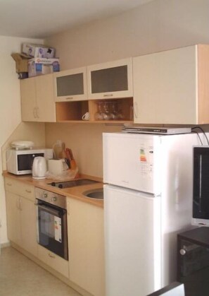 A compact kitchen with a microwave, toaster, and refrigerator. There are cabinets above the counter and a small oven to the left.