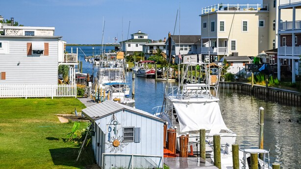 A marina with boats docked, a small house with a sun decoration, and a white fence.