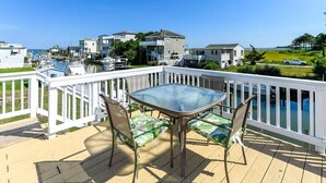 A deck with a glass-top table and chairs, overlooking a marina with boats and houses.