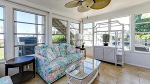 A spacious living room with large windows, a floral sofa, a glass coffee table, and a staircase leading to an outdoor area.