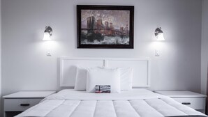 Una camera d'albergo ordinata con un letto grande, biancheria bianca, due comodini e un quadro incorniciato con una veduta della città sopra il letto.