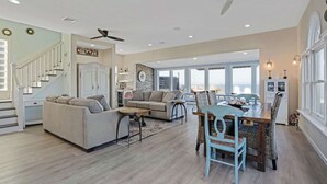 Tilava olohuone, jossa on korkea katto, ruokapöytä tuoleineen, sohva ja portaikko kaiteineen.
