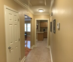 Enter a hallway leading to a kitchen area with a door, light fixture, and framed picture.