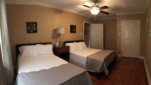 Two single beds with crisp white bedspreads and matching pillows, a ceiling fan, and framed artwork adorn this well-maintained room.