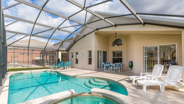 A swimming pool area with a glass-enclosed roof, lounge chairs, and a patio with a barbecue setup.