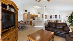 A spacious living room with a leather sofa, wooden entertainment center, and a dining area with a table and chairs.