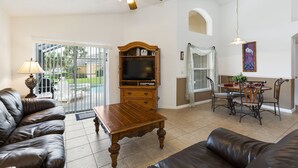 A spacious living room with leather sofas, a wooden coffee table, a ceiling fan, and a dining area with a table and chairs.