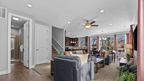 Ein geräumiges Wohnzimmer mit grauem Sofa, Deckenventilator und Blick auf die Küche und den Essbereich.