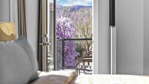 Ein Zimmer mit Bett, Fenster und Blick auf blühende, violette Bäume.