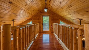 A wooden interior with a high ceiling, a central door, and a wooden railing along the walls. - 3BR Cabin Near Dollywood w/ Hot Tub, Game Room & Mountain Views |  Free ticket (Sevierville)