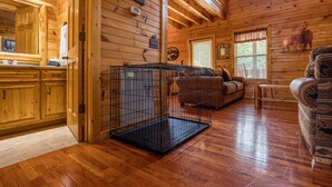 A wooden cabin interior with a wooden floor, a black metal cage, a sofa, and a window with blinds. - 3BR Cabin Near Dollywood w/ Hot Tub, Game Room & Mountain Views |  Free ticket (Sevierville)