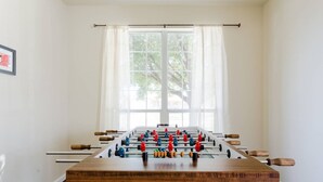 A foosball table in a room with a large window and white walls. - 5 Bedrooms - Spacious & Clean + Game Room (Austin)
