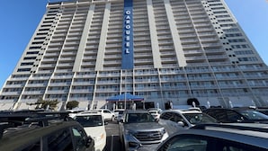 A high-rise building with a prominent 'CAROUSEL' sign, multiple balconies, and a parking lot with various vehicles. - Oceanfront and Bay view at the Carousel with indoor pool (ocean city)