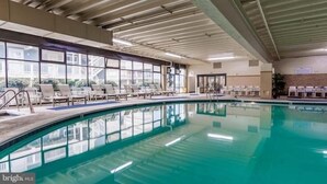 An indoor swimming pool with lounge chairs and a view of buildings outside. - Oceanfront and Bay view at the Carousel with indoor pool (ocean city)