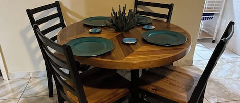A round wooden dining table with four chairs, a centerpiece, and a white cabinet in the background.