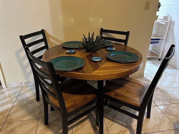 A round wooden dining table with four chairs, a centerpiece, and a white cabinet in the background.