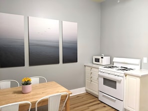 A modern kitchen with white appliances, a wooden dining table, and three large abstract paintings on the wall.