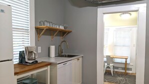Una cucina compatta con lavastoviglie integrata, macchina del caffè e lavello. Sopra il lavello, una mensola in legno con bicchieri.