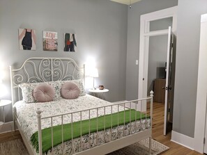 A bedroom with a white metal bed frame, floral bedding, a green throw, and a nightstand with a lamp.