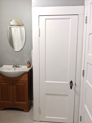 A bathroom with a white sink, wooden cabinets, a mirror, and a white door.