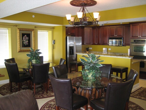 A dining area with a round table and chairs, a chandelier, and a kitchen with wooden cabinets and modern appliances.