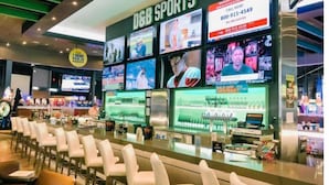 A sports bar with multiple screens displaying sports events, a bar area with stools, and a counter with a cash register. - Jeffscondos --- Ocean Blue Resort - Ocean Front vacation rental 5bed / 4bath (Myrtle Beach)