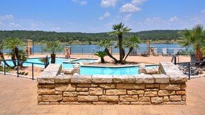 Zona de piscina con muros de piedra, palmeras y vistas a un lago y colinas.