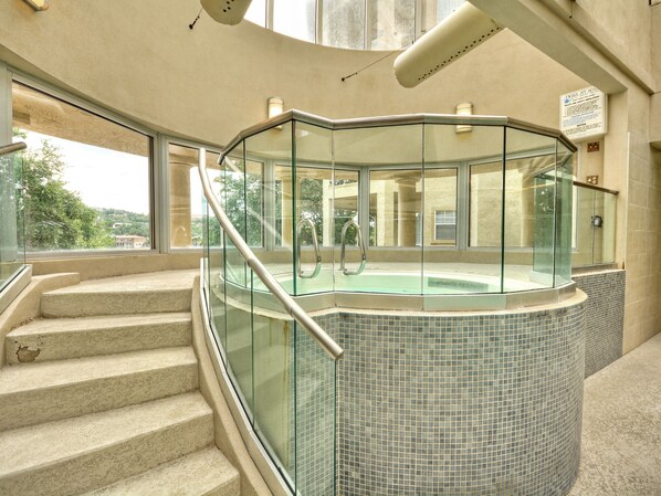 Un jacuzzi con paredes de vidrio y revestimiento de azulejos, junto a una escalera que lleva a un nivel superior.