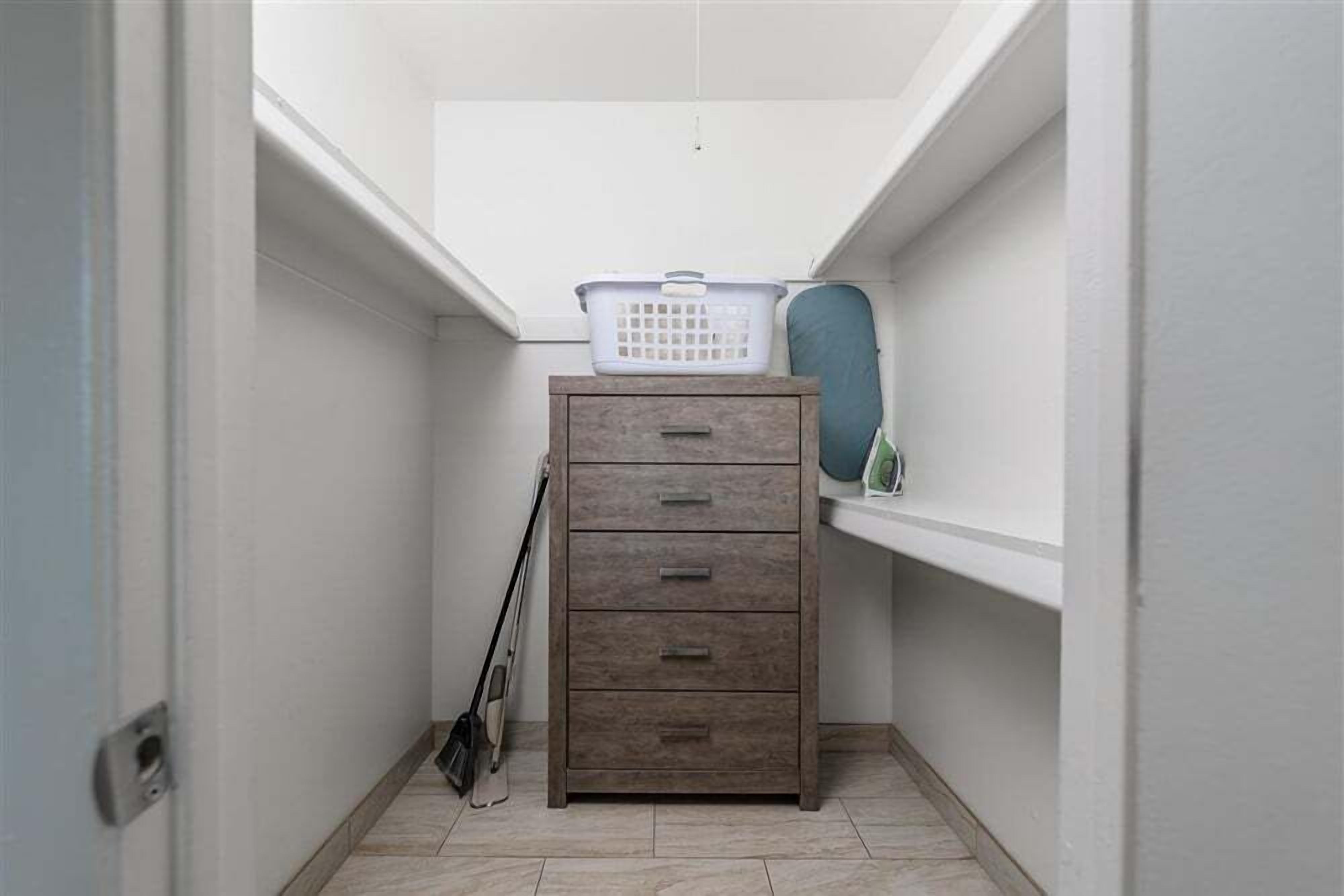 Een smalle gang met een houten kast, een wasmand erbovenop en een bezem die tegen de muur staat.
