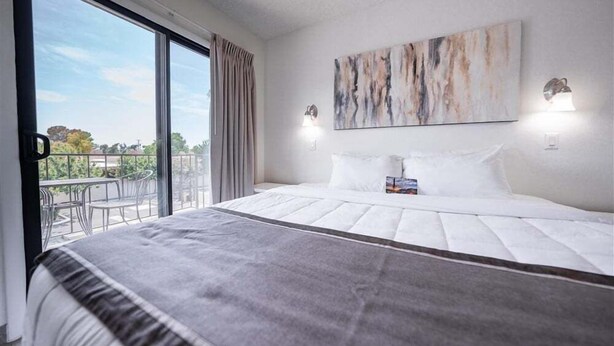 A hotel room with a large bed, a balcony with a view, and a painting on the wall. - 219 Fully Furnished, WiFi Included! (Scottsdale)