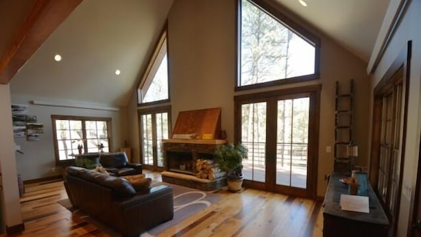 A spacious living room with a fireplace, large windows, and a high ceiling.
