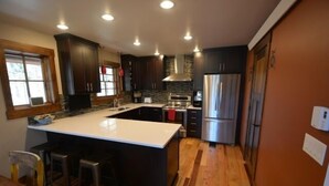 A modern kitchen with dark cabinetry, a central island, stainless steel appliances, and wooden flooring.