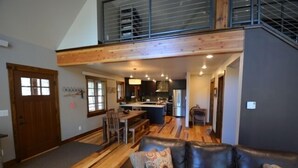 A spacious living area with a high ceiling, a dining table, and a kitchen in the background.