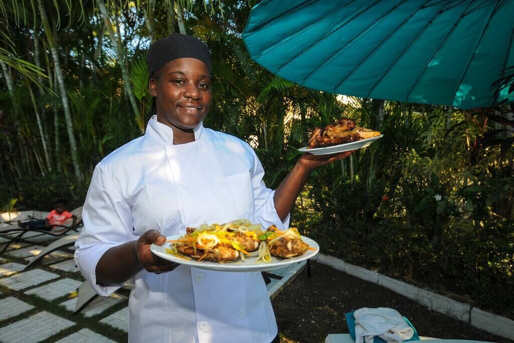 Un chef sostiene un plato de comida al aire libre, bajo un paraguas verde.